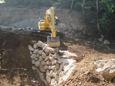 Pelle posant un enrochement de soutènement en forêt