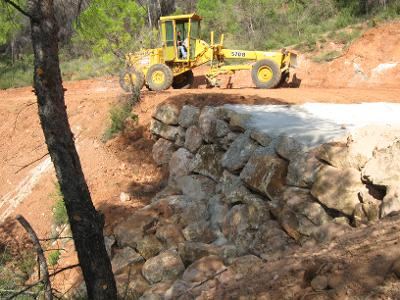 Niveleuse au-dessus d'un enrochement de talus forestier